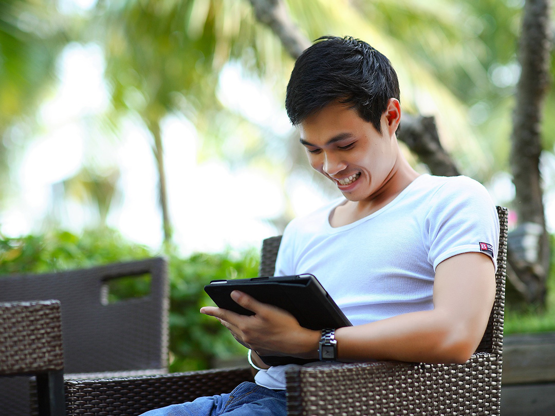 Editorial photo: Asian youth sitting at an outdoor lounge, looking at a tablet